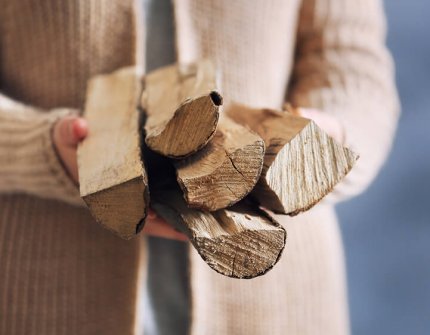 Woman in beige cardigan carrying wood in her hands